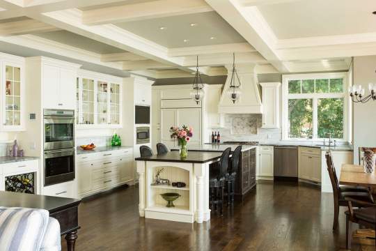 This kitchen is a comfortable and functional space, complete with white appliances, two dining tables, and a center island with a vase of flowers.
